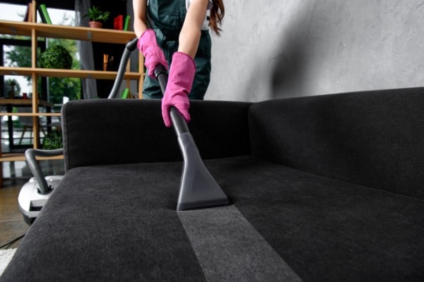 partial view of woman in rubber gloves cleaning furniture with vacuum